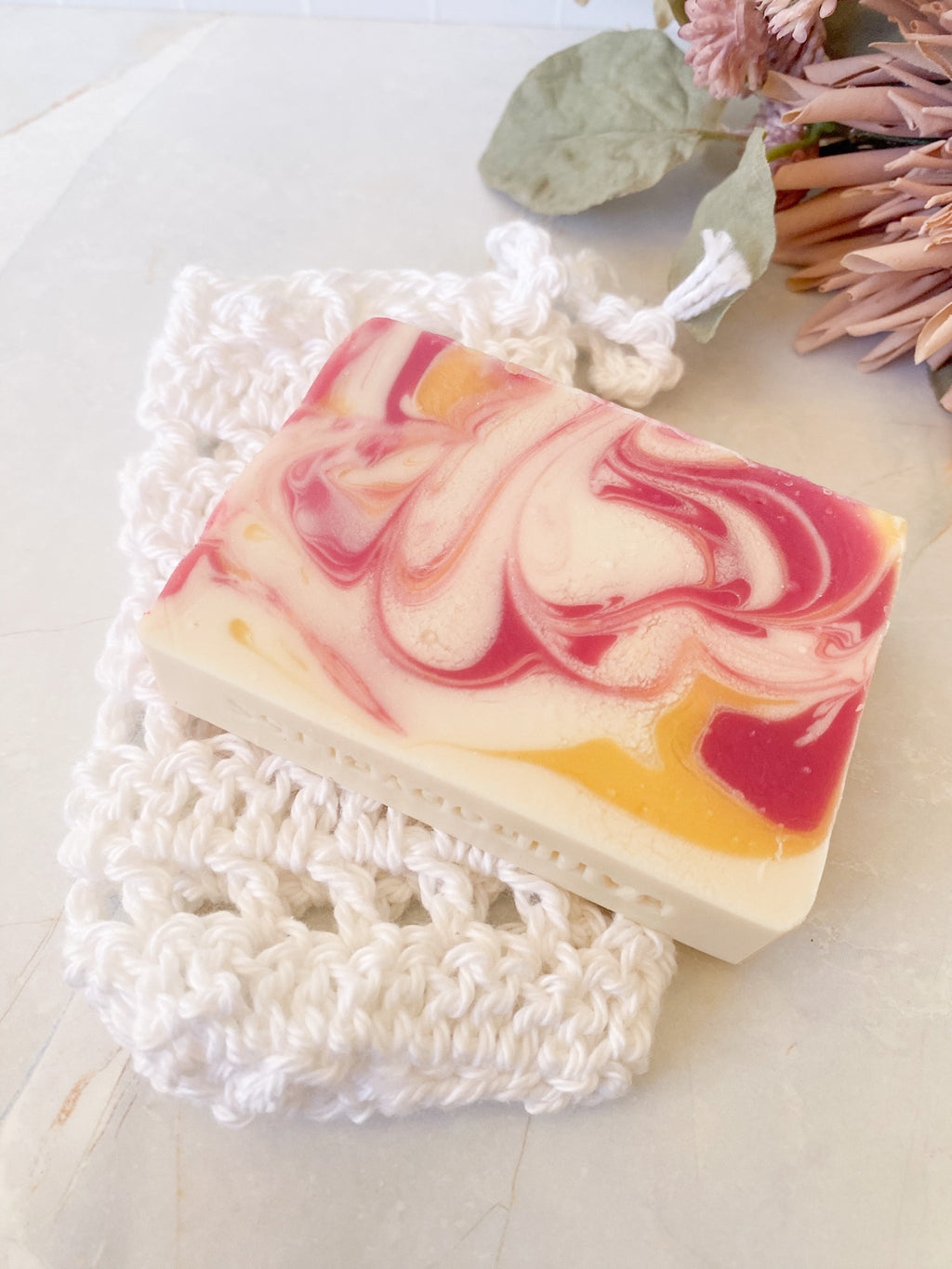 Swirled soap bar with pink and yellow on a white hand crochet soap saver sack