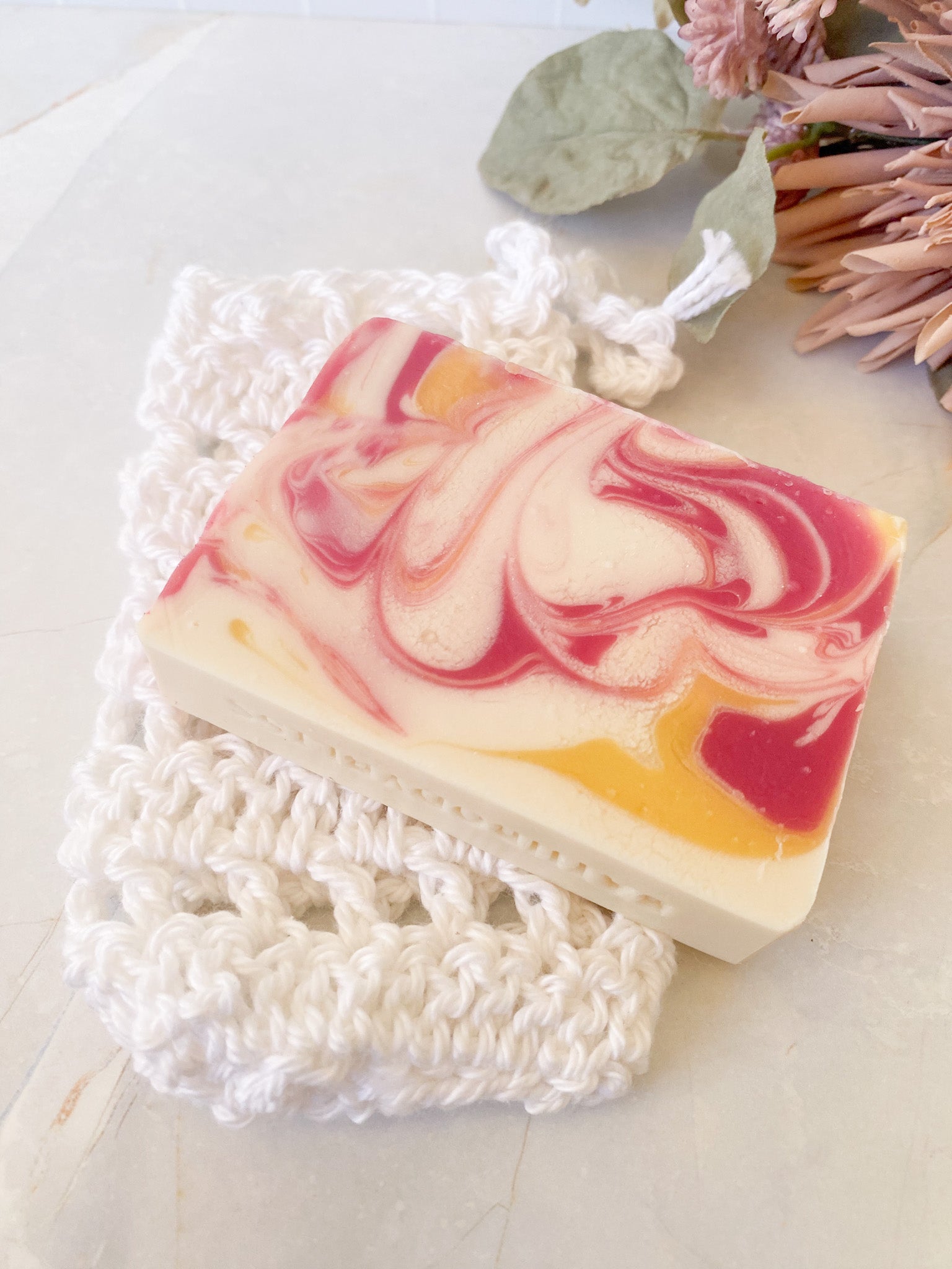 Swirled soap bar with pink and yellow on a white hand crochet soap saver sack