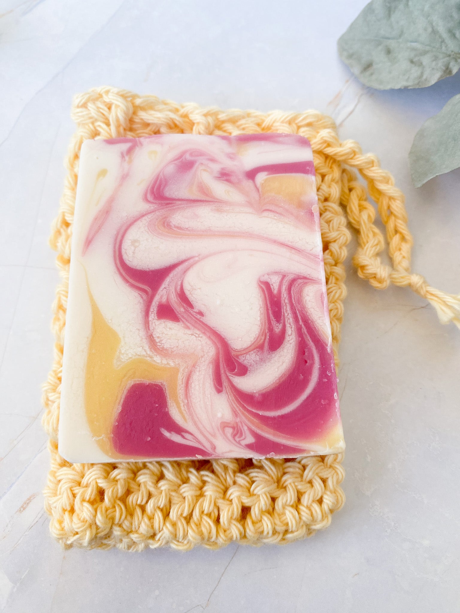 Swirled pink and yellow soap bar on a hand crochet yellow soap sack with a light background