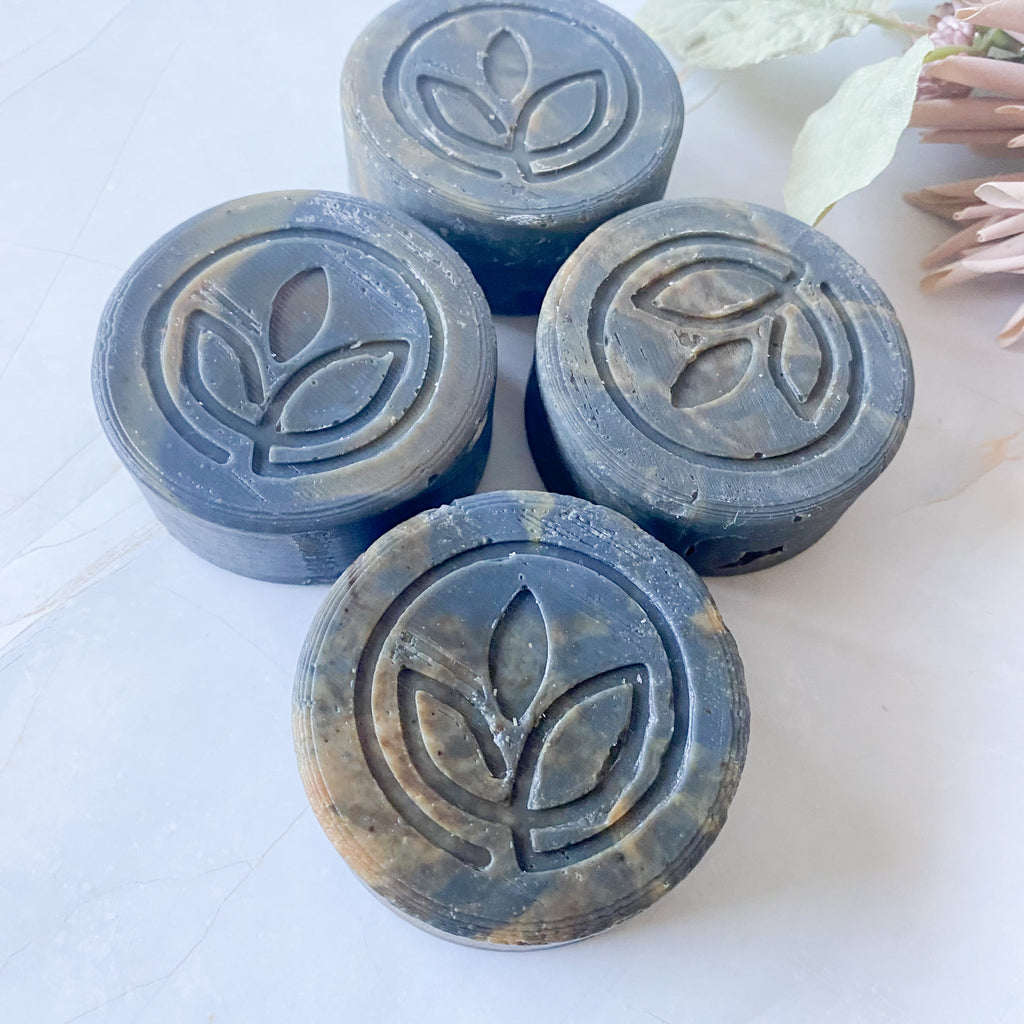 Four dark grey swirled soap bars with a leaf logo on a pale surface