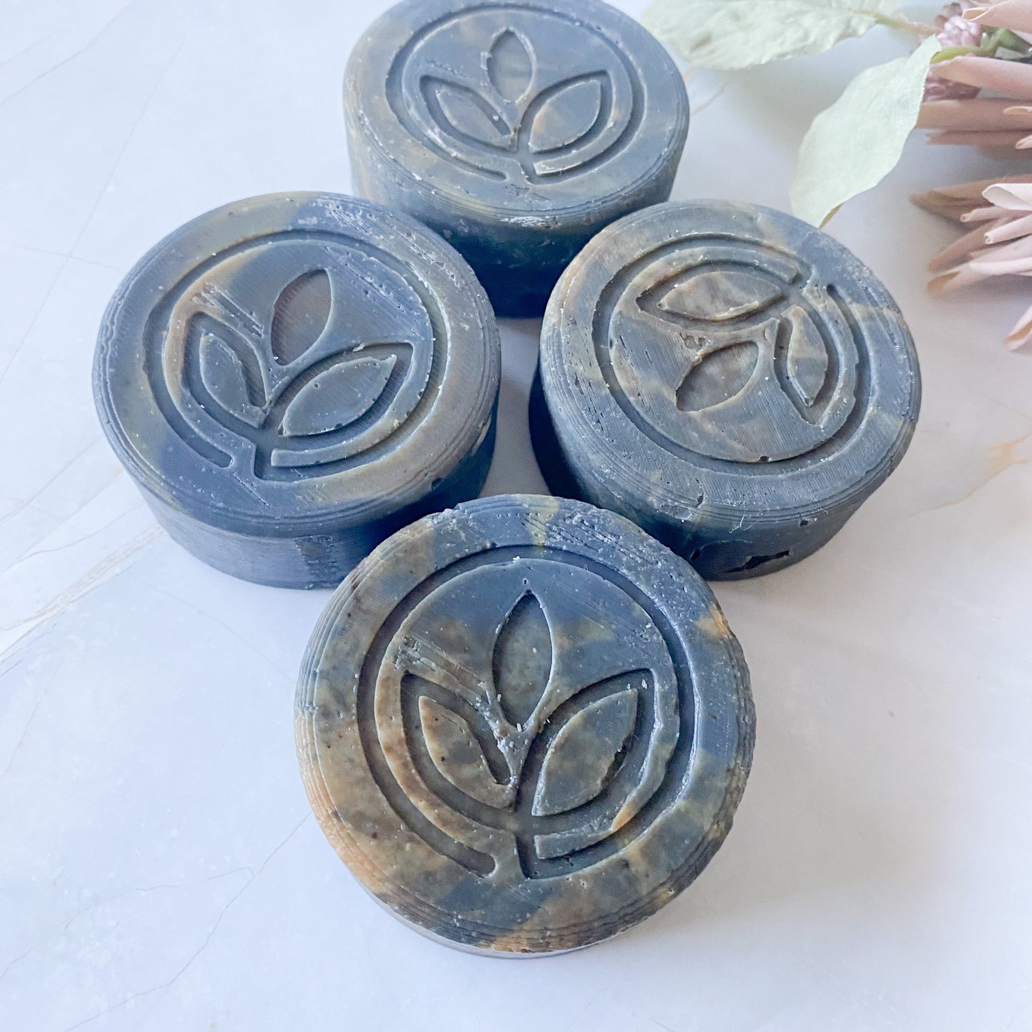 Four dark grey swirled soap bars with a leaf logo on a pale surface