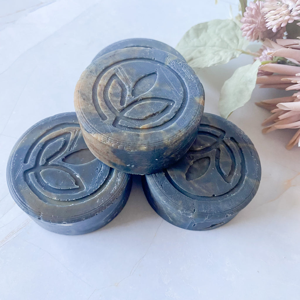 stack of four dark grey swirled round soap bars with leaf design on a light surface