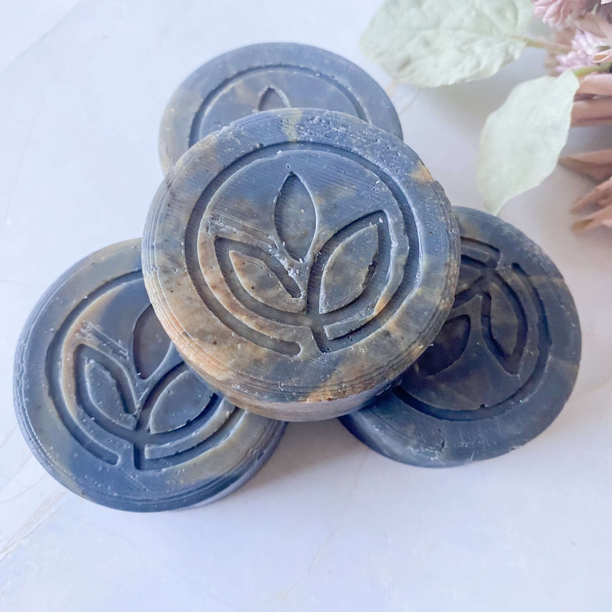 Three circular black swirled soap bars with a leaf logo on a white background