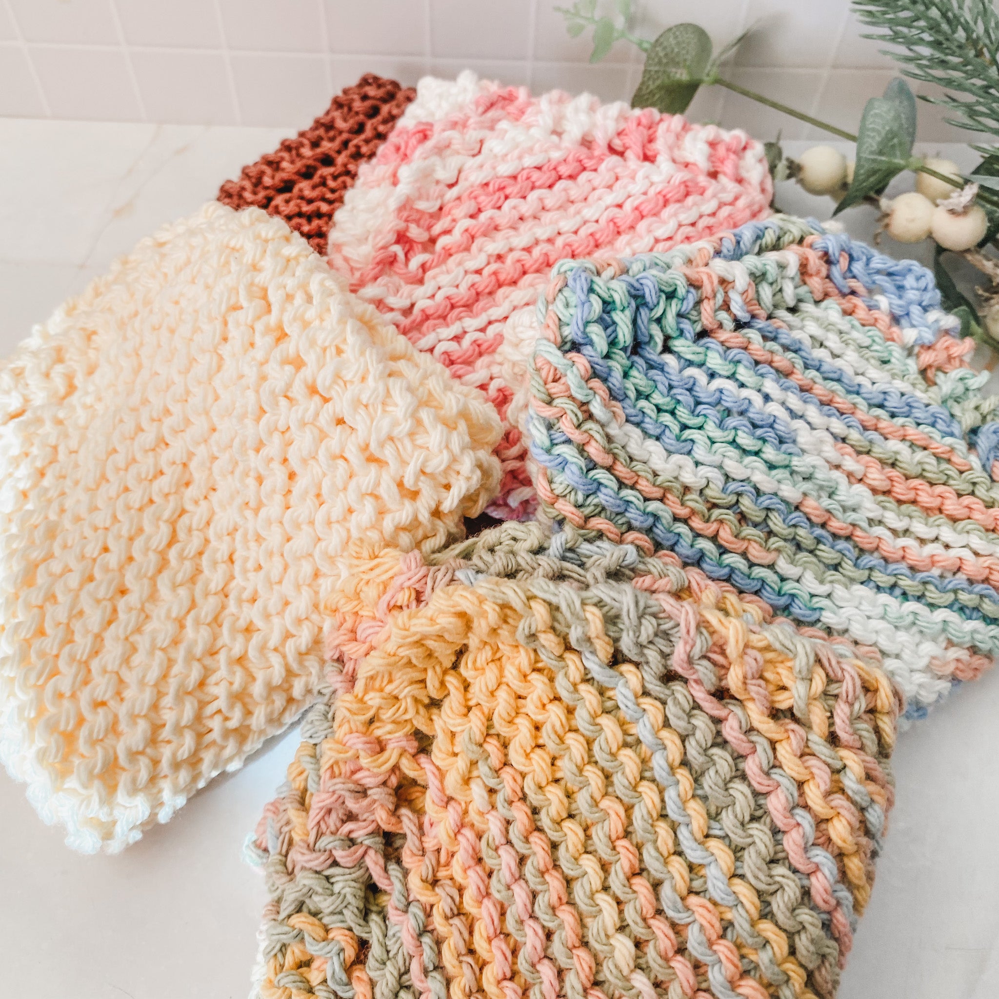 Stack of colorful knitted dishcloths on a white surface with a light background