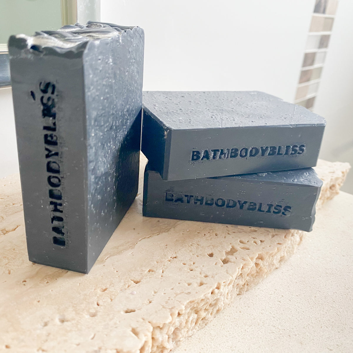 Three gray soap bars with 'BathBodyBliss' branding on a marble surface.
