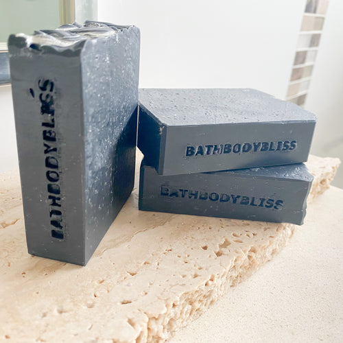 Three gray soap bars with 'BathBodyBliss' branding on a marble surface.