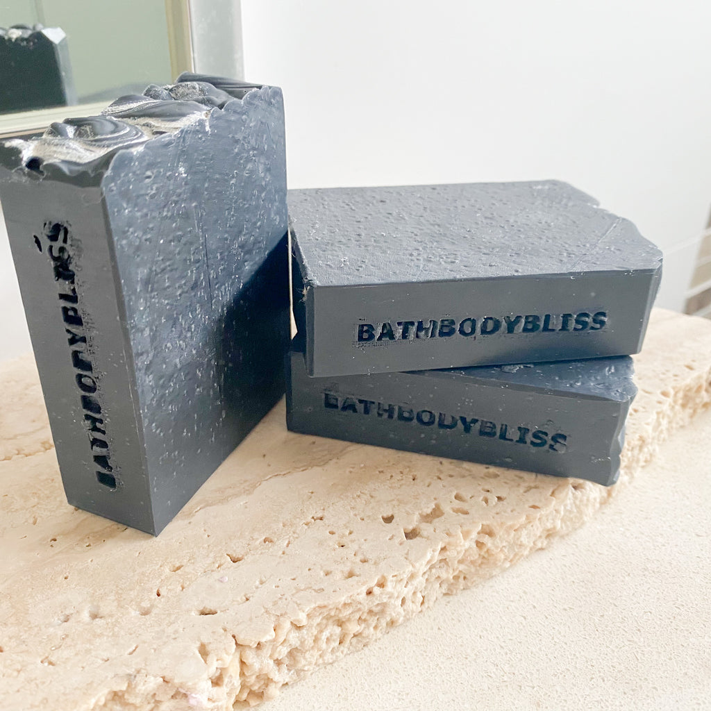 Three bars of BathBodyBliss dark grey soap on a textured surface
