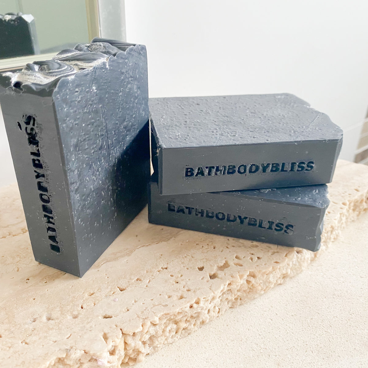 Three bars of BathBodyBliss dark grey soap on a textured surface