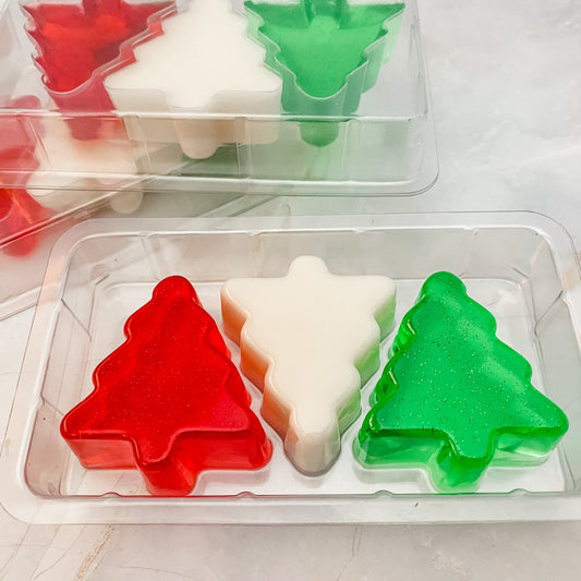 three clear packs containing three guest soaps shaped like christmas trees, in translucent red, translucent green and plain white