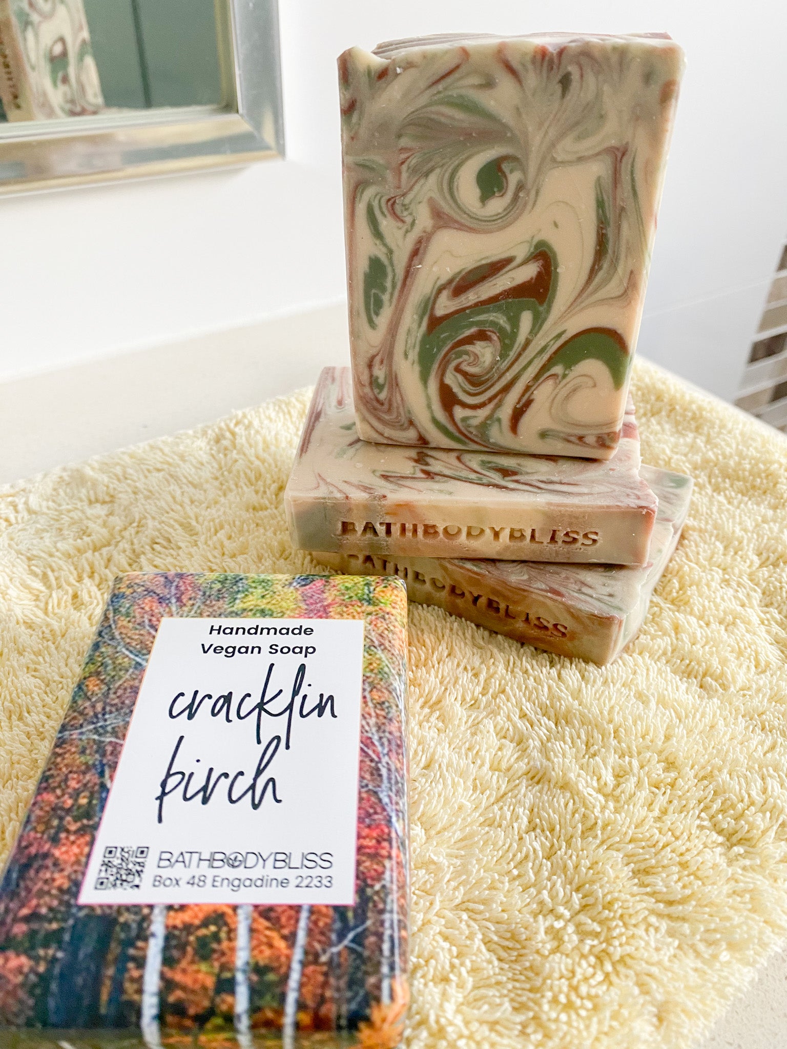A bar of Cracklin' Birch fragranced soap with a swirl pattern featuring green and brown colors, placed on a white surface, with its packaging that reads 'Bath Body Bliss' and the product name.