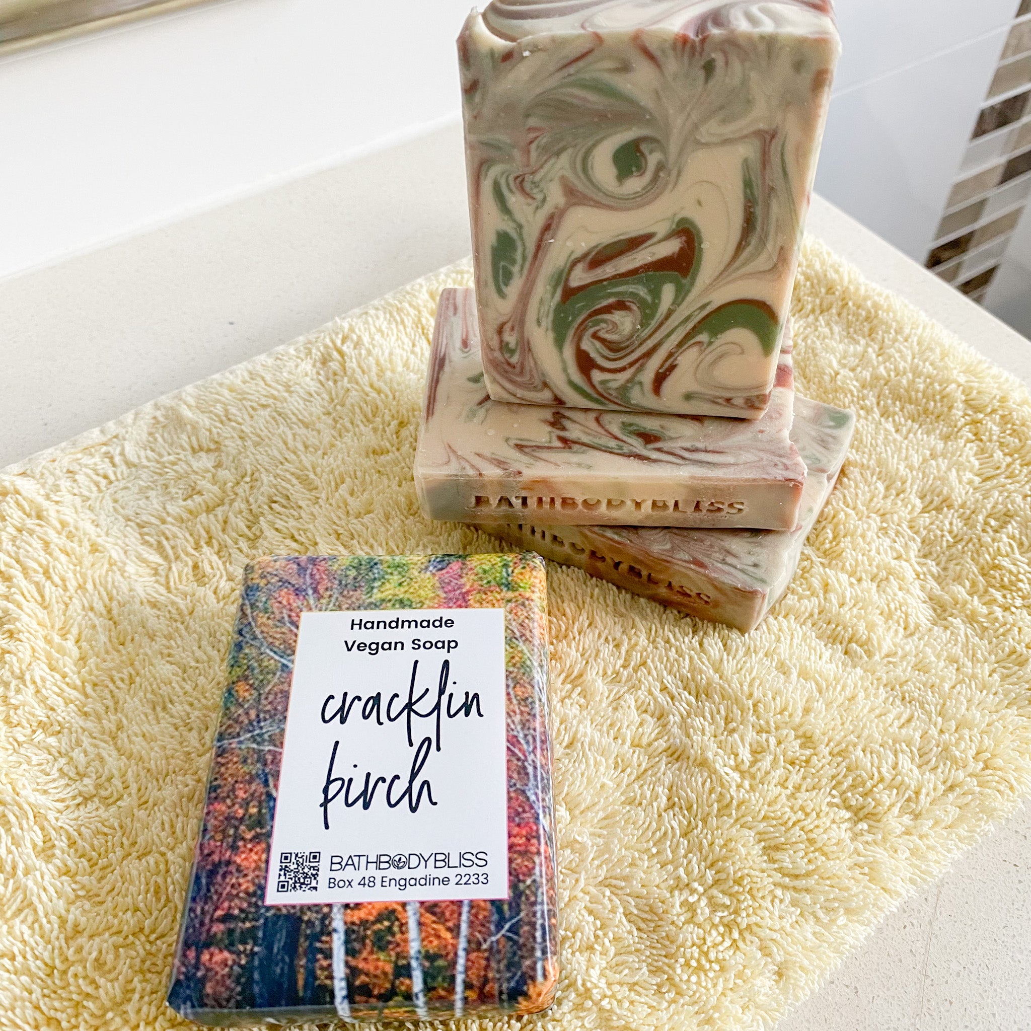 unwrapped swirled soap bars and a wrapped cracklin birch labelled soap on a yellow towel