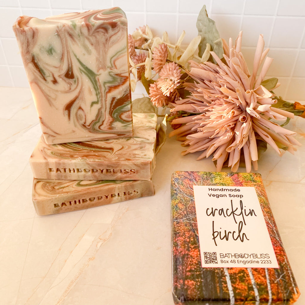 three swirled unwrapped soap bars and a wrapped cracklin birch by bath body bliss soap bar on a light background with floral decor