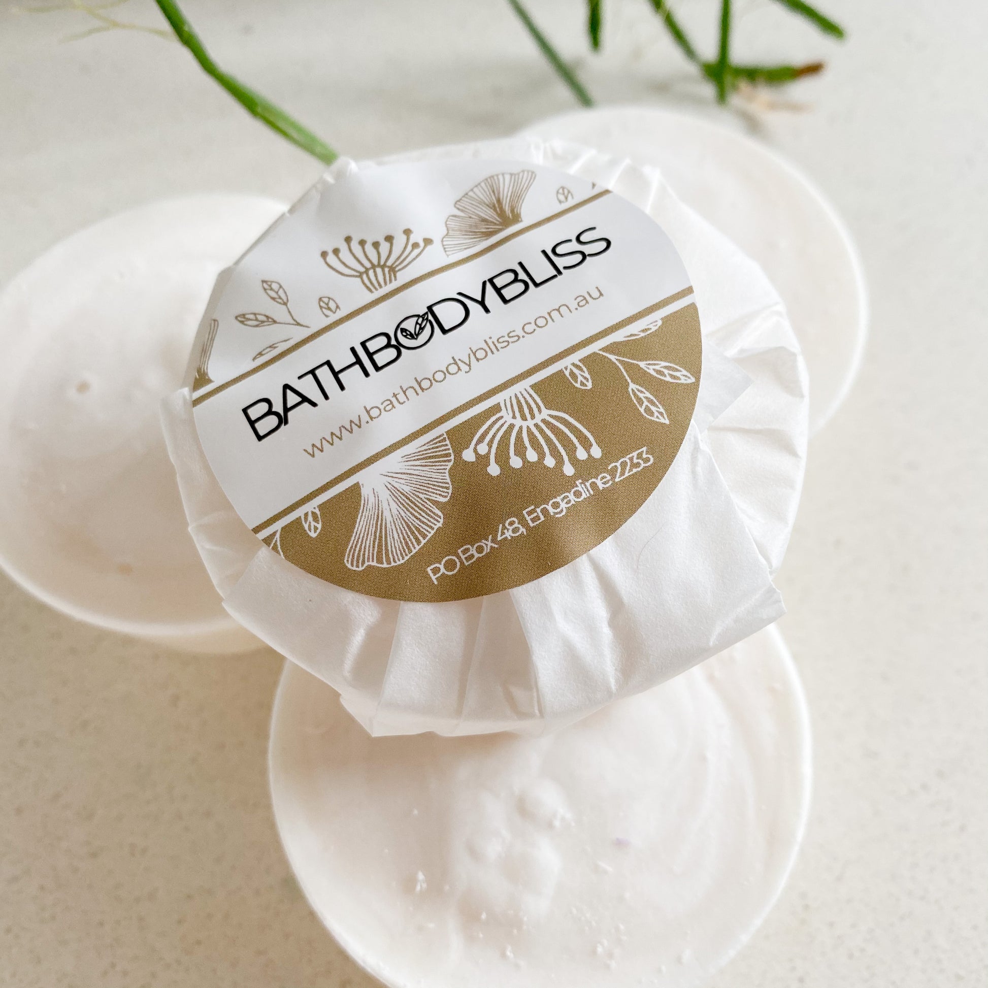 stack of round white soaps with bathbodybliss label on a pale background