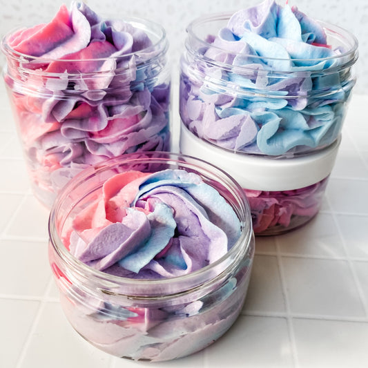 four jars of multi coloured whipped soap on a light tiled background