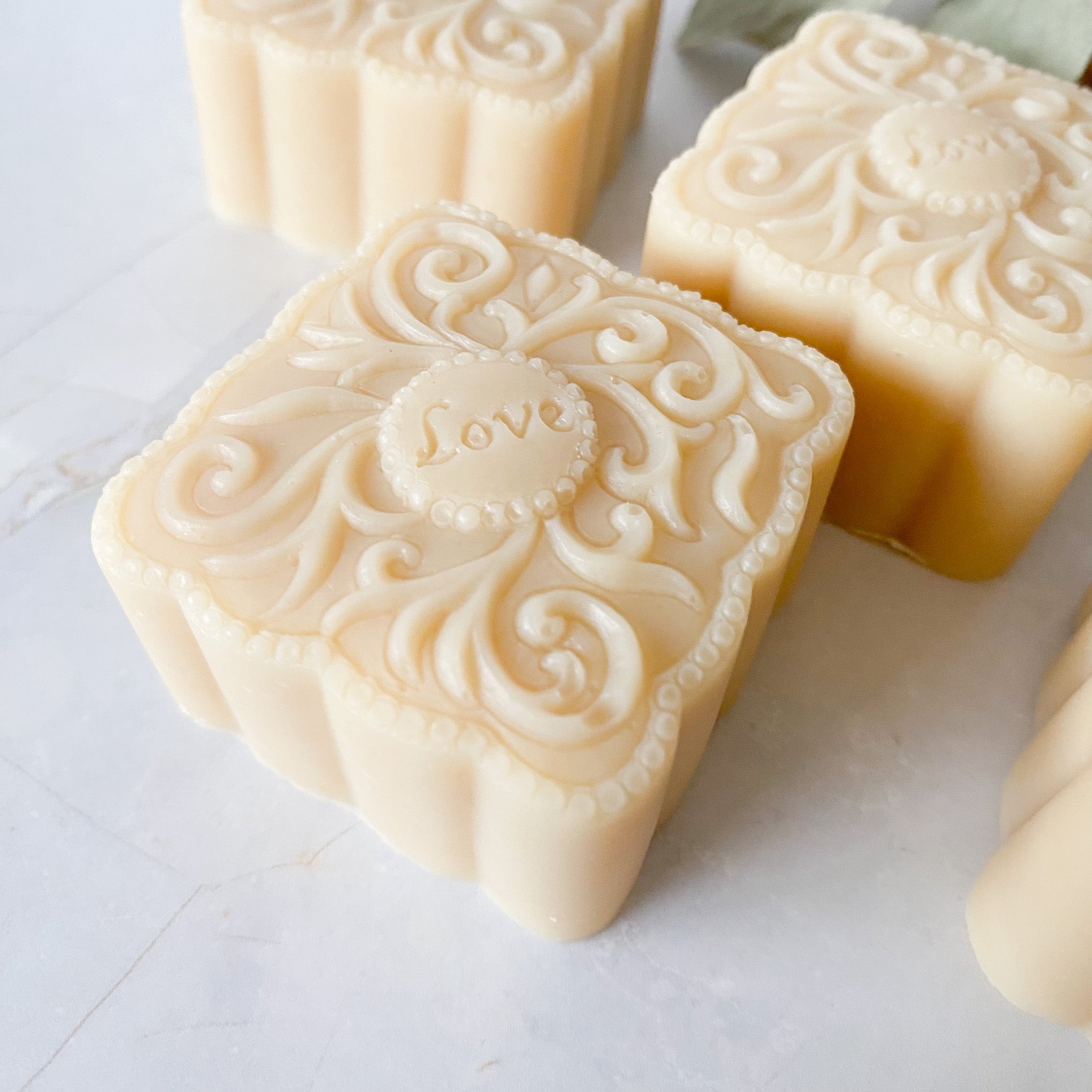 Three square bars of soap with decorative patterns on a light surface