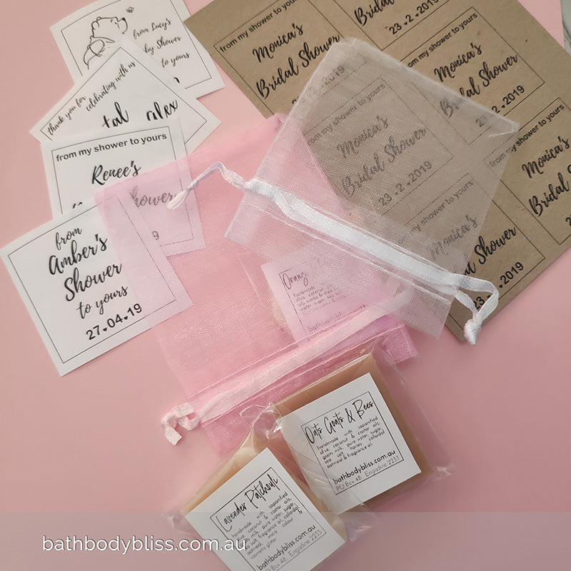 small soap pieces with personalised abels and organza bags on a pink surface