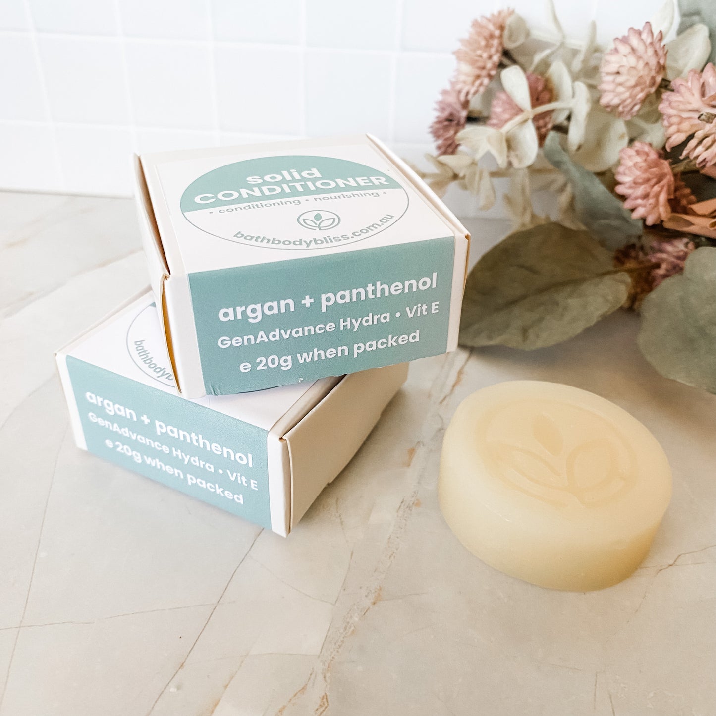 Solid conditioner bar and packaging on a light surface with flowers in the background