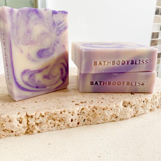 three bars of purple and white swirled soap with bathbodybliss stamp, arranged on a stone surface