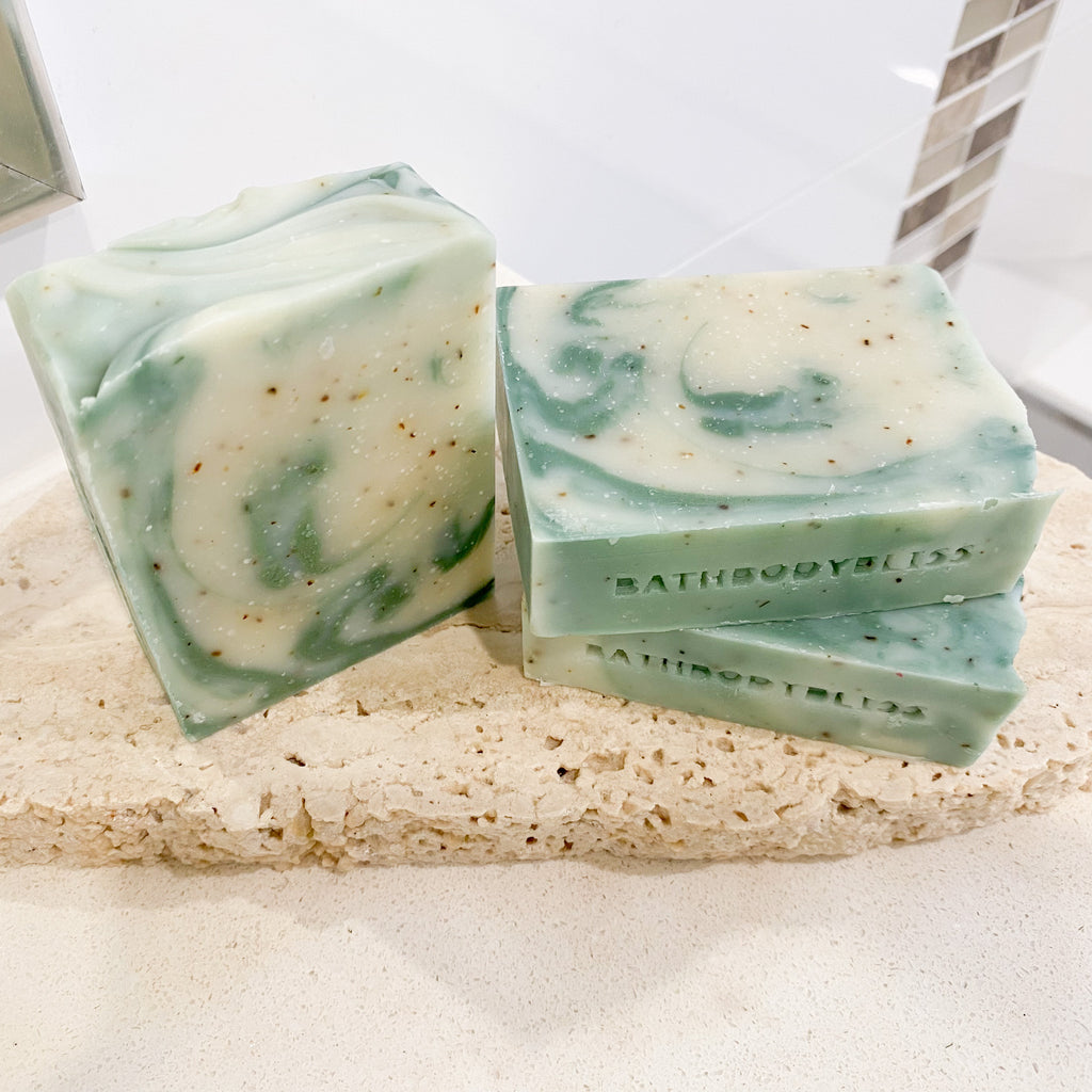 three bars of green and white swirled soap with speckles of green tea leaves & bathbodybliss branding, arranged on a stone surface