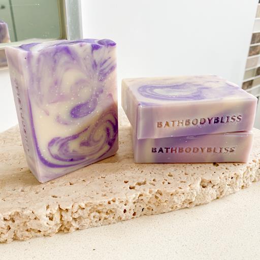 three bars of purple and white swirled handmade soaps arranged on a stone surface