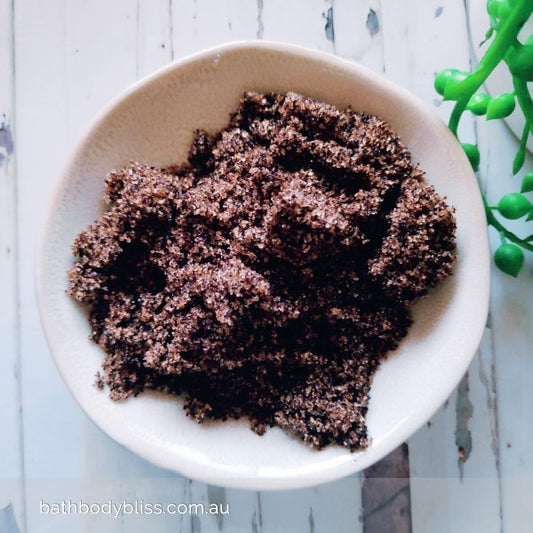 white bowl of coffee body scrub on a pale wooden background with bathbodybliss logo