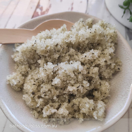 speckled bowl filled with pale green sugar body scrub, with a bamboo spoon