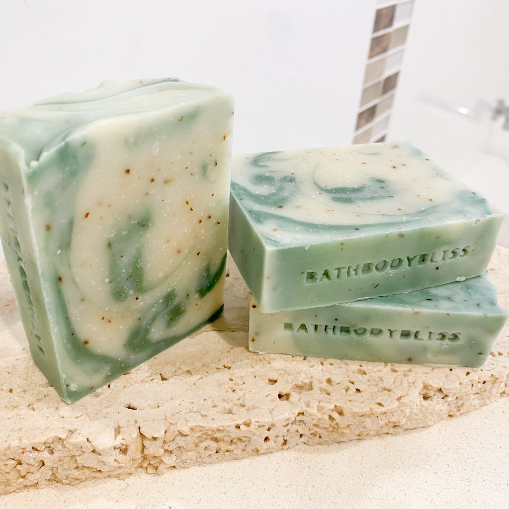 three bars of green and white swirled handmade soap with bath body bliss stamp, arranged on a stone surface