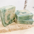 three bars of green and white swirled handmade soap with bath body bliss stamp, arranged on a stone surface
