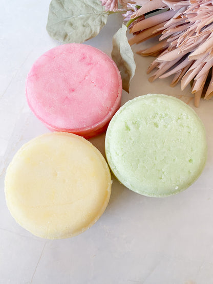 Three colorful shampoo bars on a light surface with decorative elements.