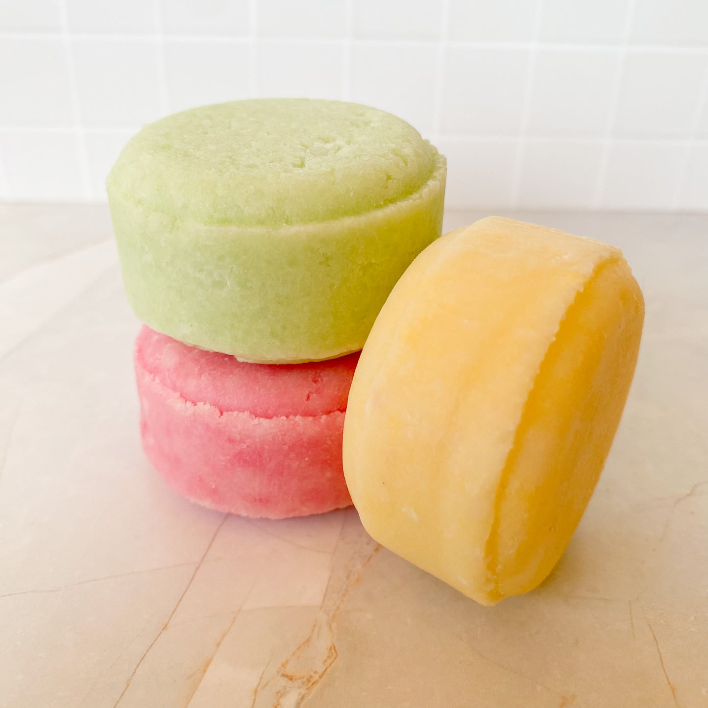 Three colorful shampoo bars stacked on a marble surface