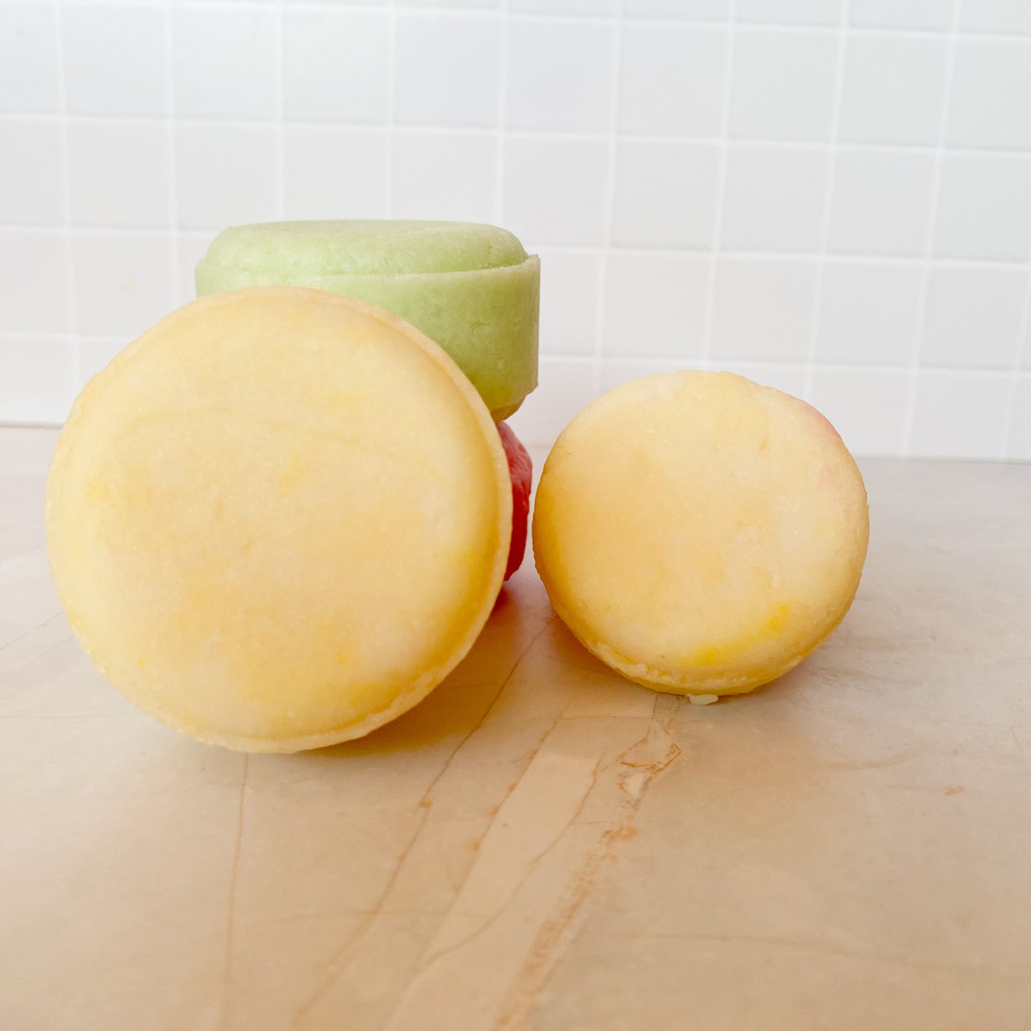 yellow green and pink shampoo bars on a marble surface with white tiles in the background