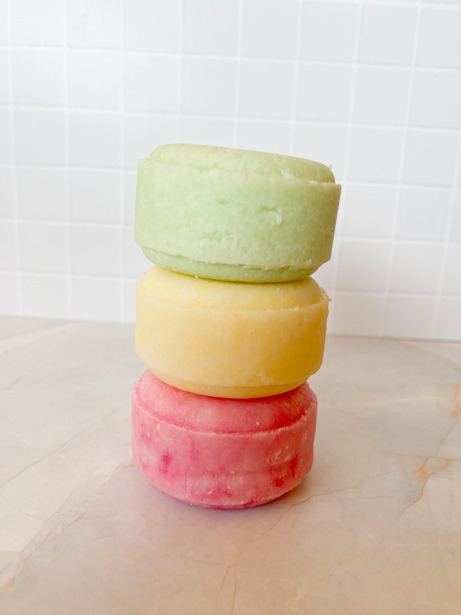 Stack of three colorful shampoo bars on a marble surface with a tiled wall background.