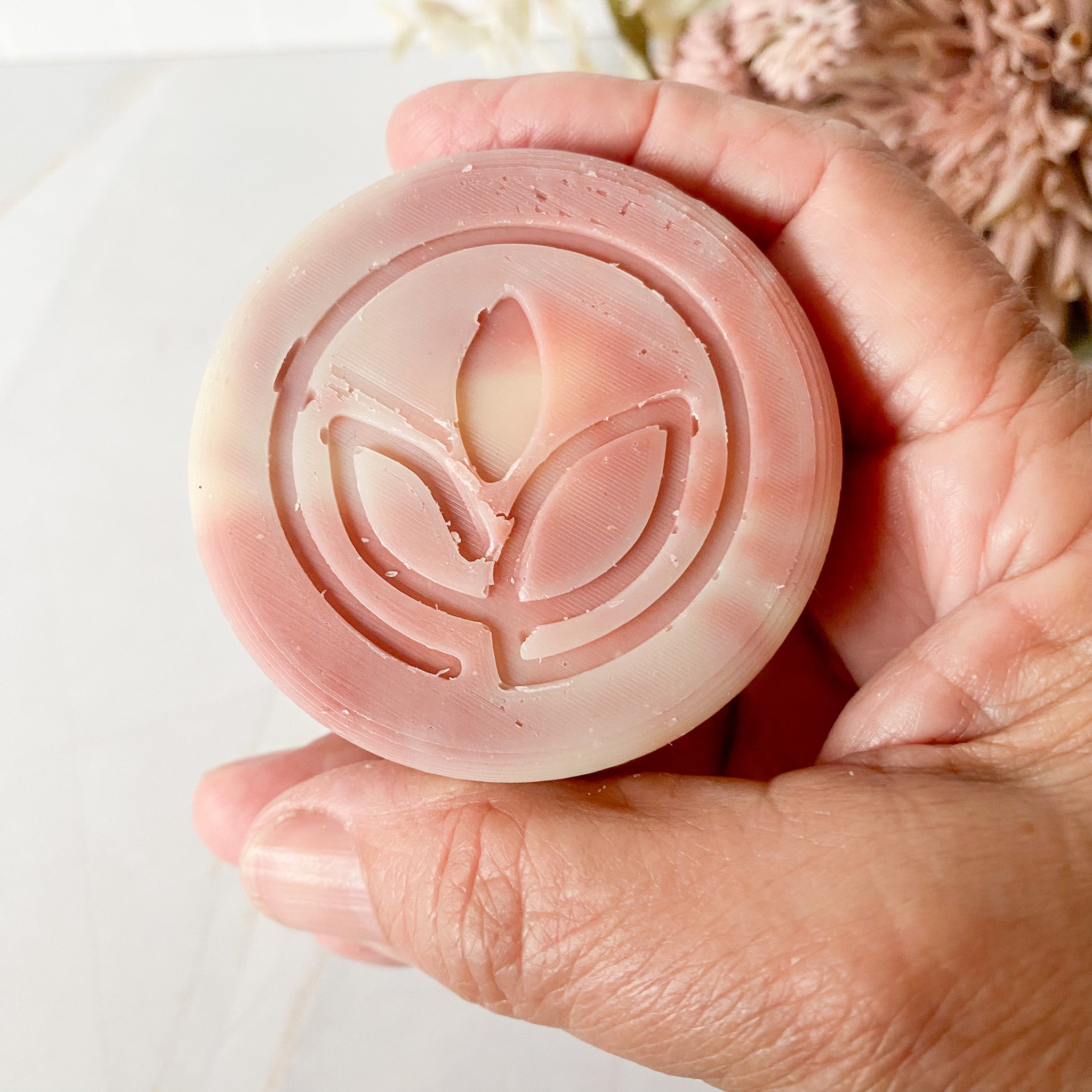 Hand holding a swirled pink soap bar with a leaf design on a light background