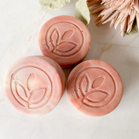 Three round pink swirled soap bars with a leaf design on a light background