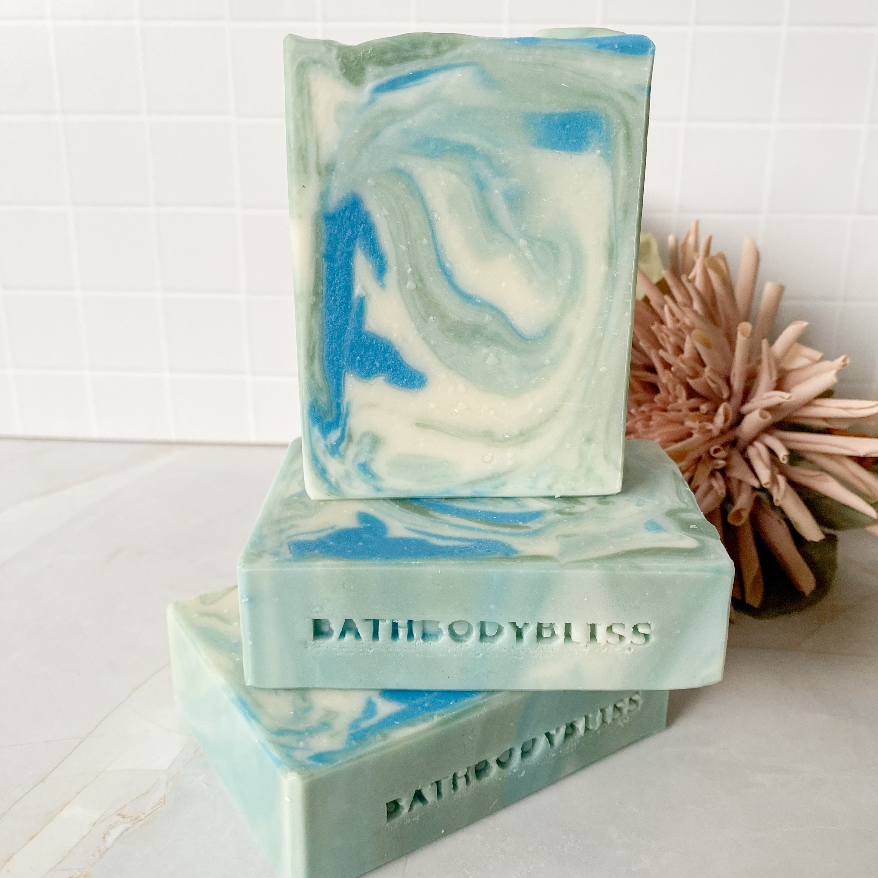Three swirled soap bars from BathBodyBliss on a white surface with a decorative flower.