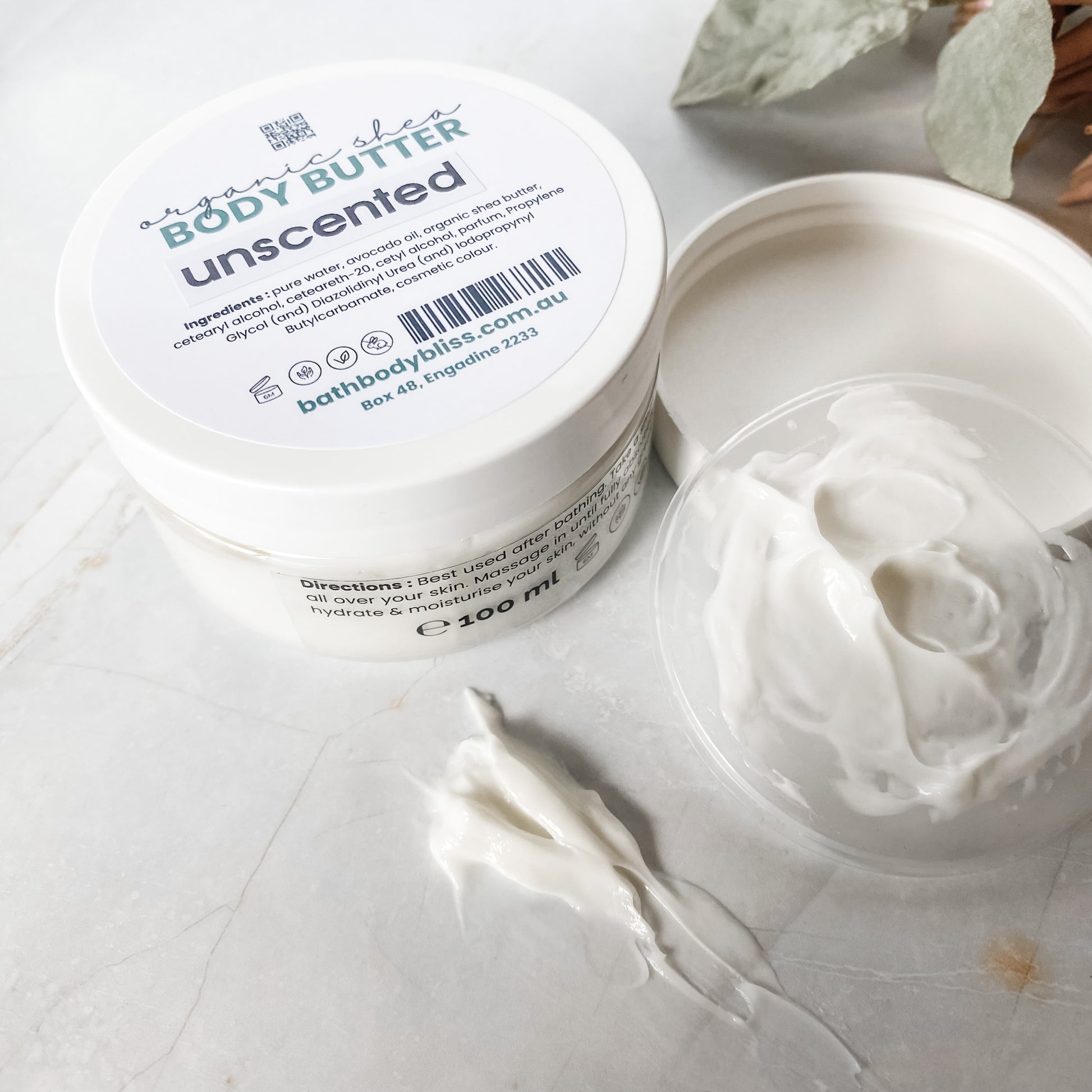 opened bathbodybliss body butter container with smear of white body butter on a light marble background