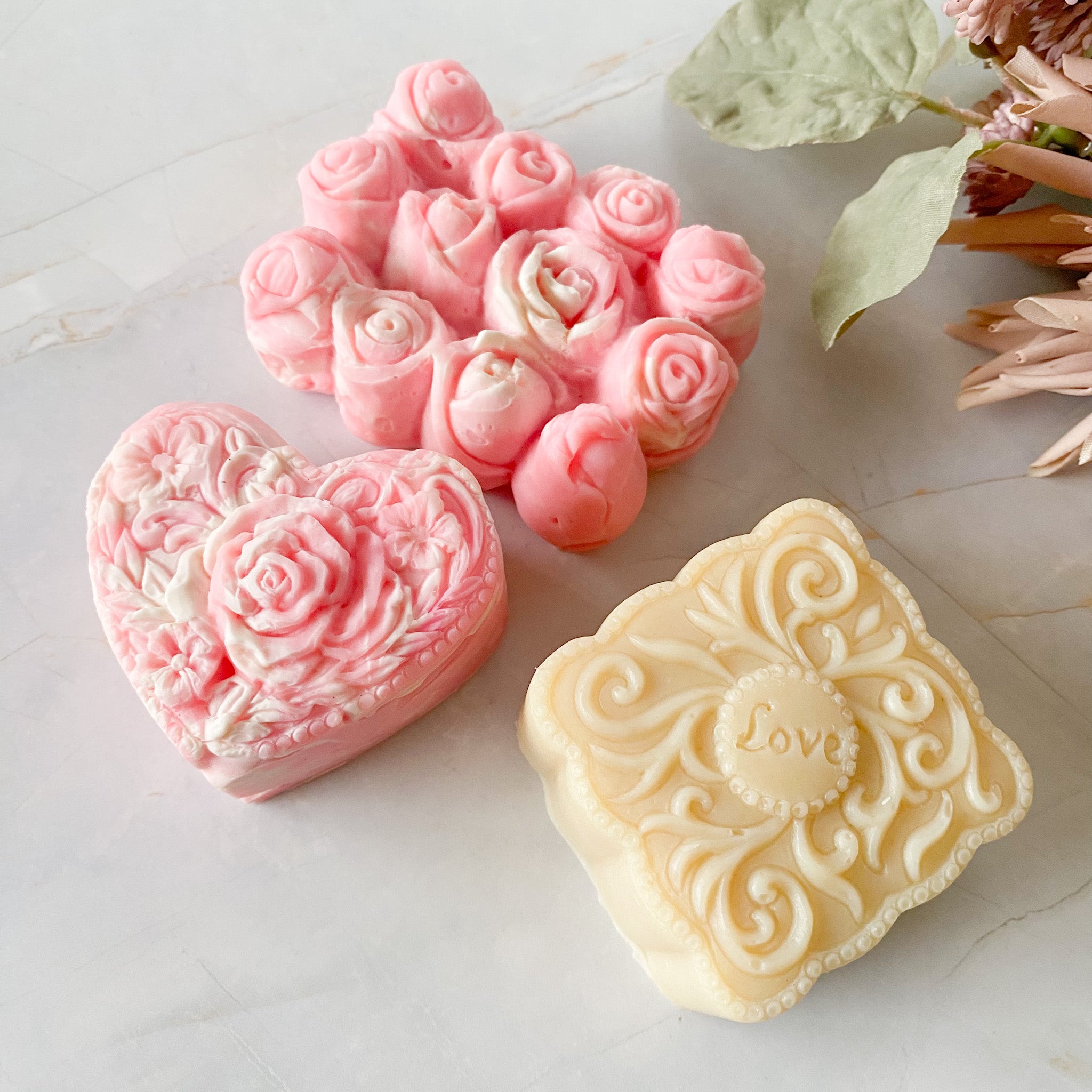 Three decorative soaps with floral and heart designs on a marble surface.