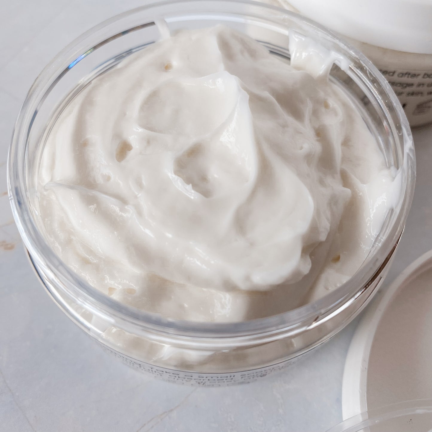 opened jar of thick, white body butter on a pale background