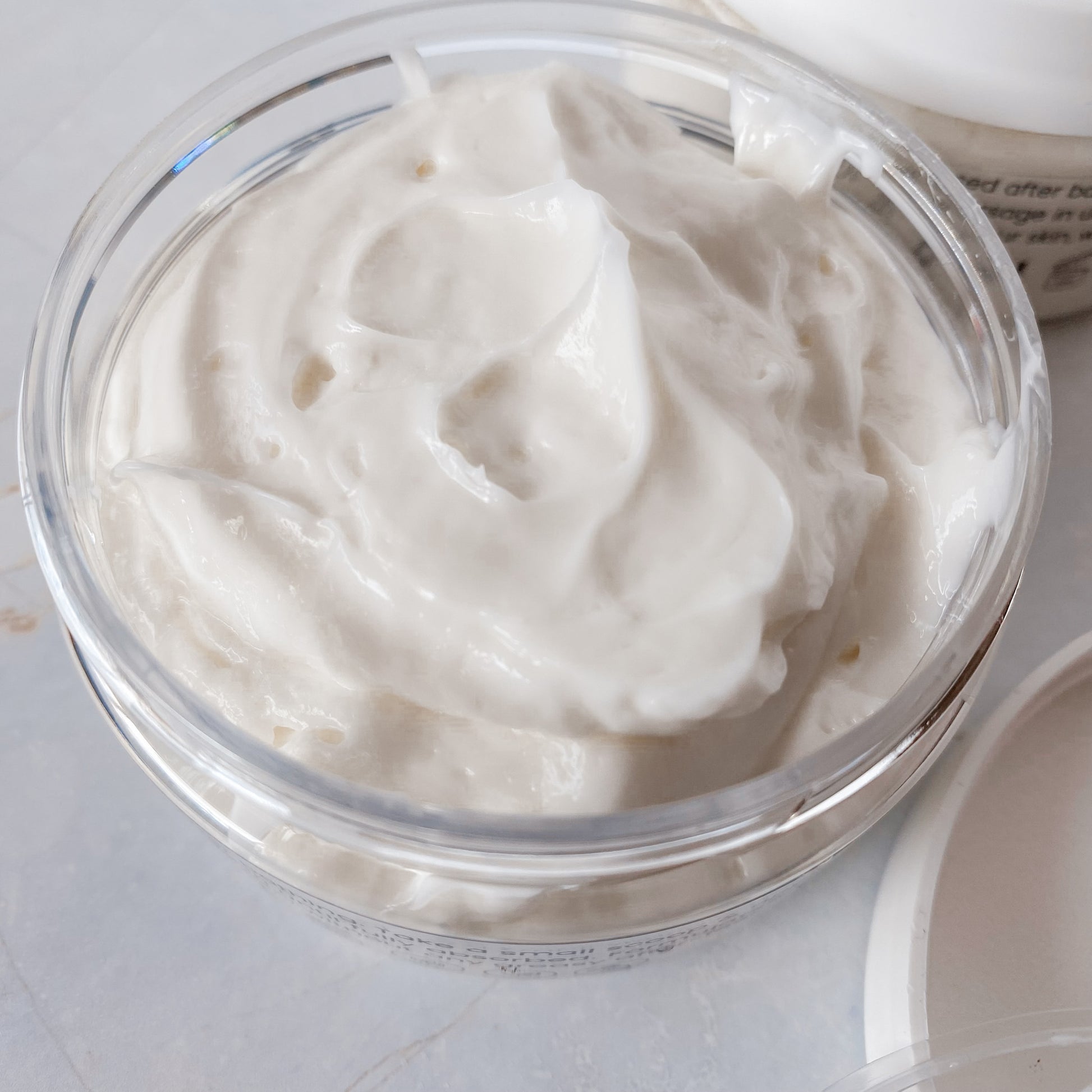 opened jar of thick, white body butter on a pale background