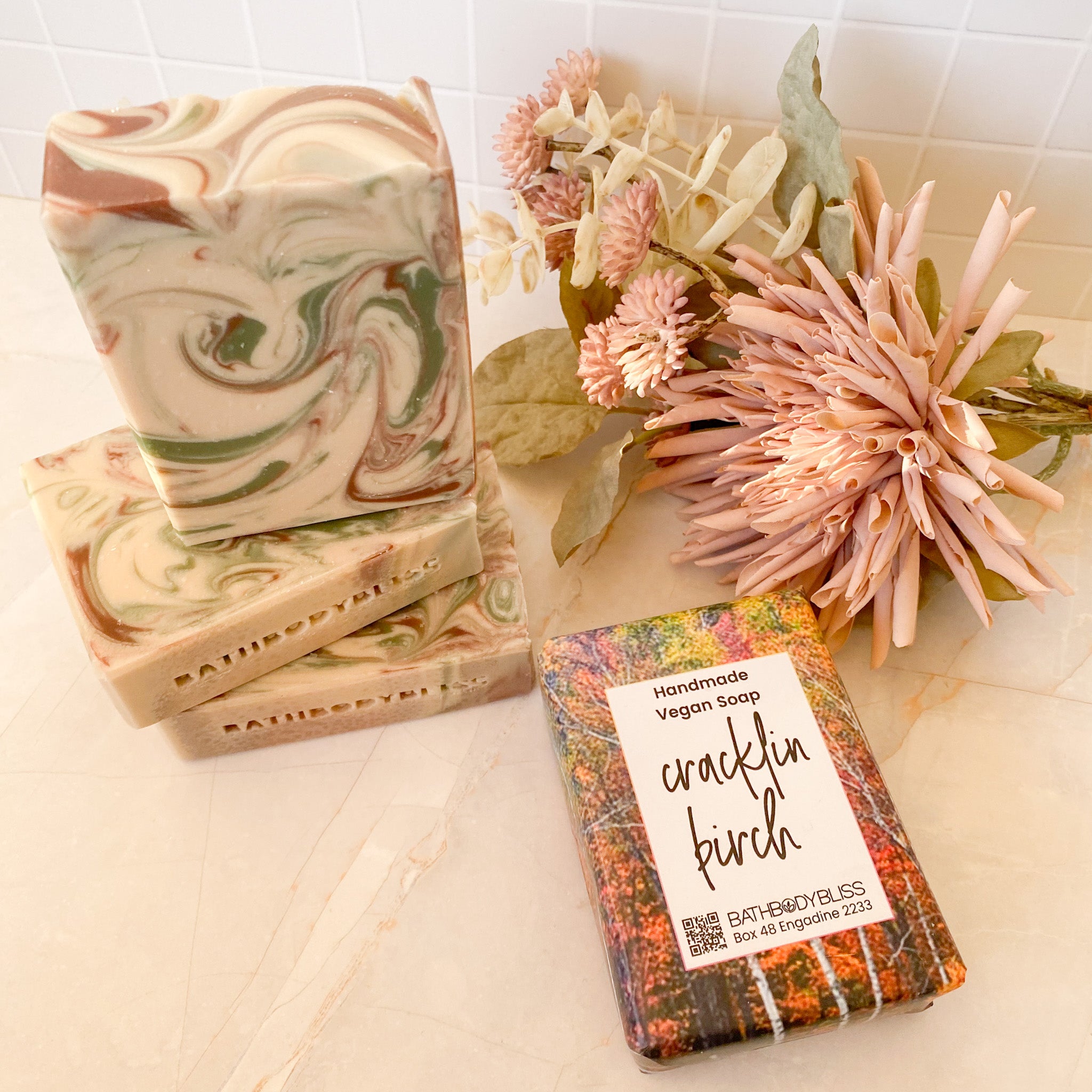 three swirled unwrapped soap bars and a wrapped soap bar on a light surface with floral decor