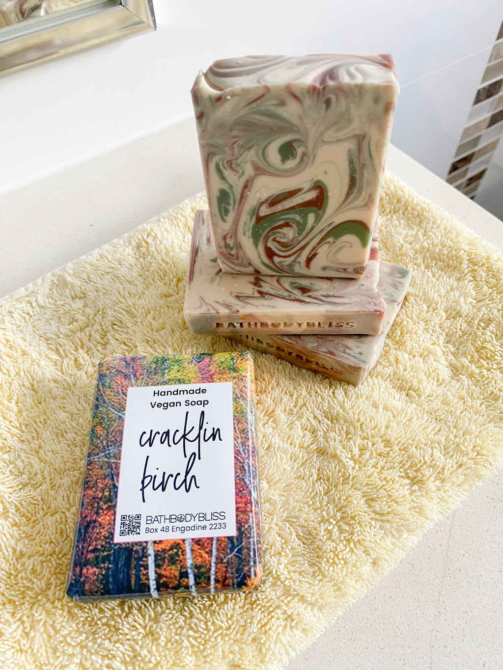 three unwrapped soap bars and a wrapped cracklin birch soap bar on a yellow handtowel