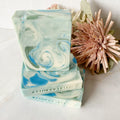 Stack of swirled blue, green and white soap bars with a pink flower on a white surface