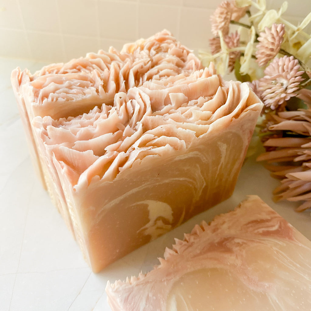 Bar of soap with floral design on a white surface with flowers in the background