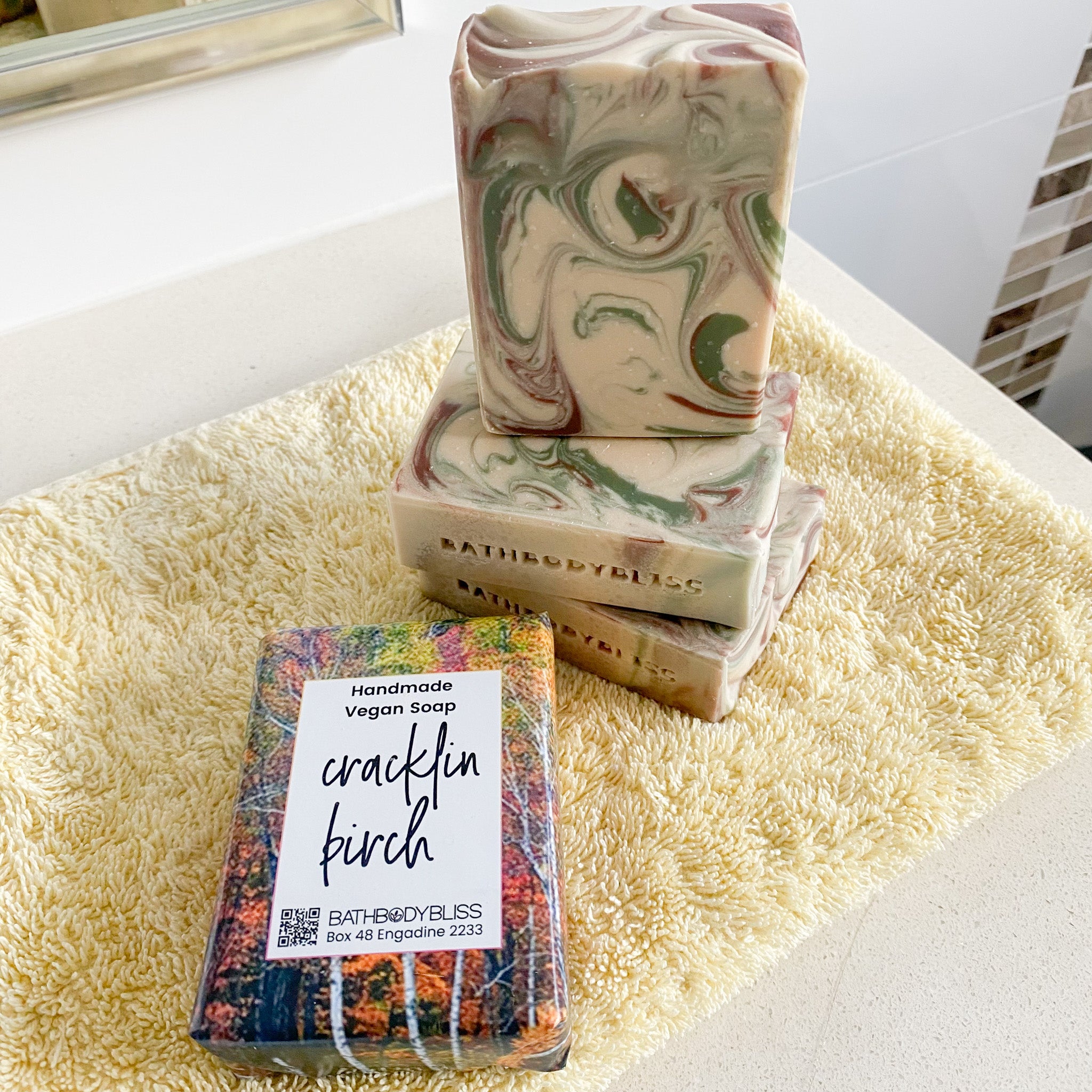 three unwrapped swirled soap bars and one wrapped cracklin birch soap bar on a yellow towel
