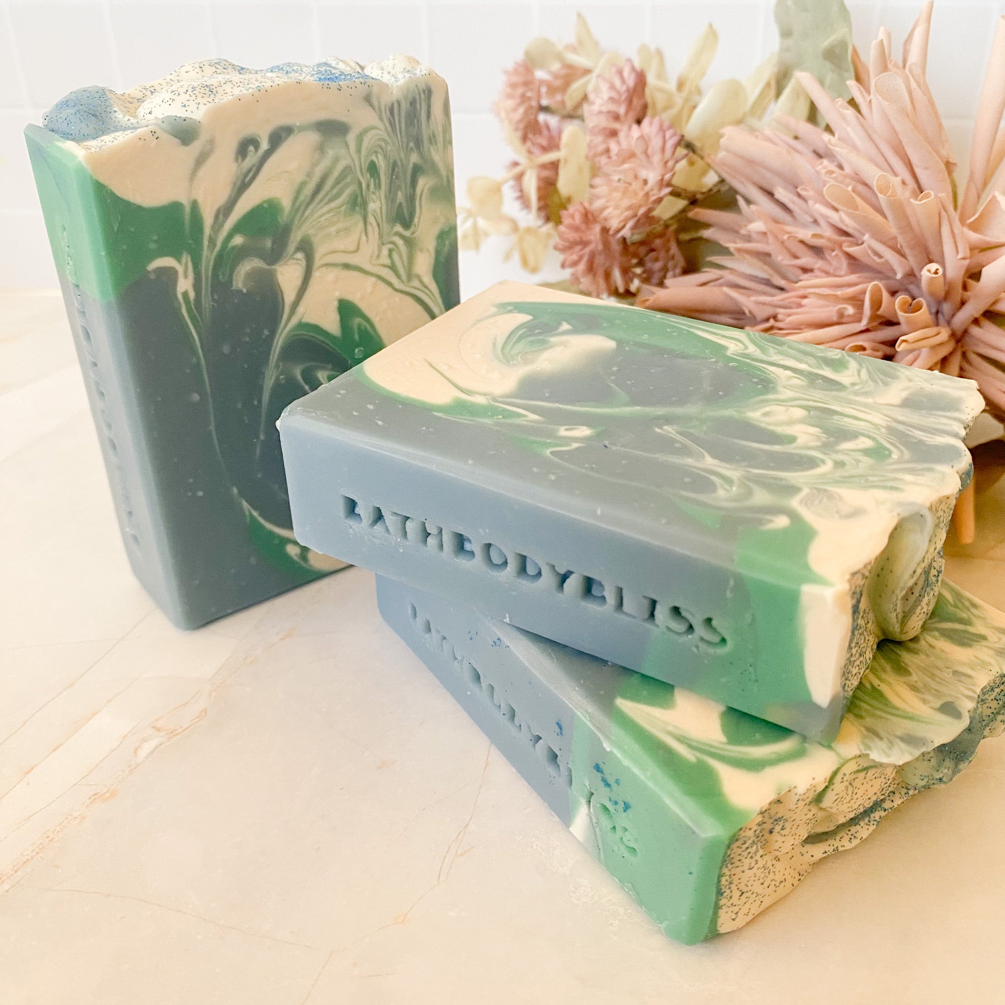 swirled blue, green and white soap bars with 'BathBodyBliss' branding on a light surface.