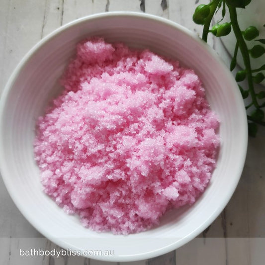 white bowl filled with pink sugar bodyscrub on a pale background & a plant in the corner