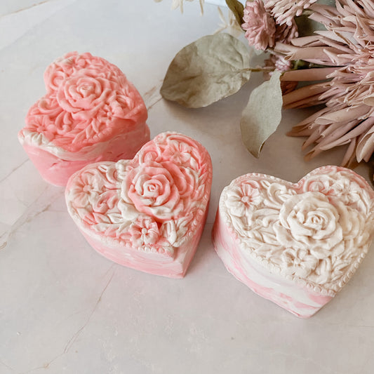 Three heart-shaped floral soap bars on a light surface with dried flowers and leaves.