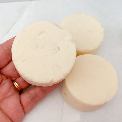 Three round, handmade shampoo soap bars held in a hand on a light background
