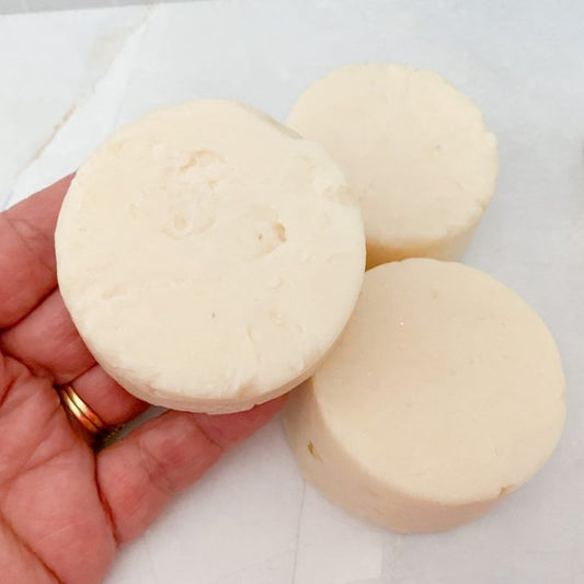 Three round, handmade shampoo soap bars held in a hand on a light background