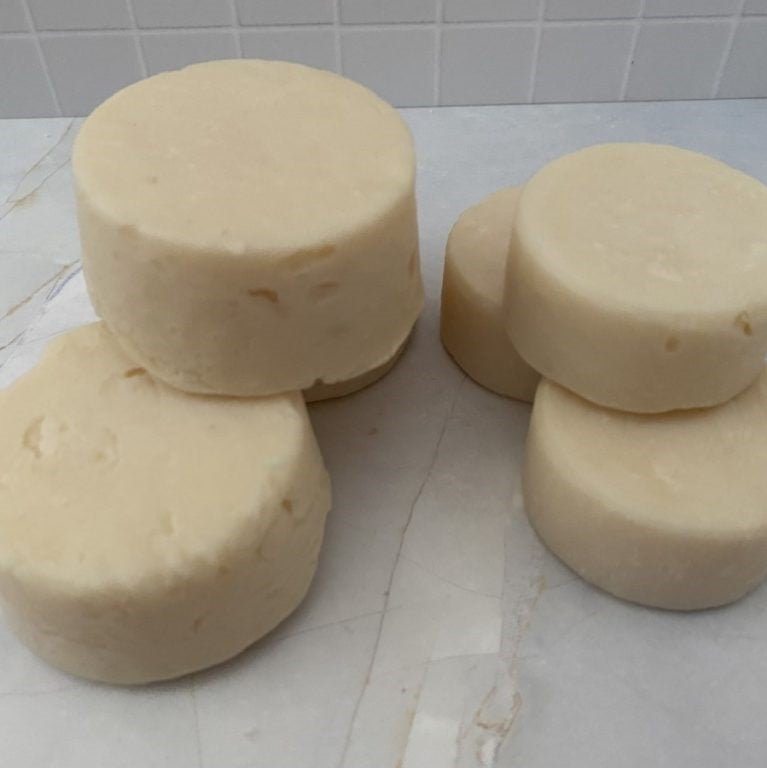 three large and 3 small handmade round shaped shampoo soap bars stacked on a tiled surface